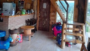 A rustic cabin interior with a kitchen area, a dining table, and a staircase leading to a loft. - Chale Sol Nascente, comfort where you can only find it here in the middle of Nature.home (Bateias de Baixo)