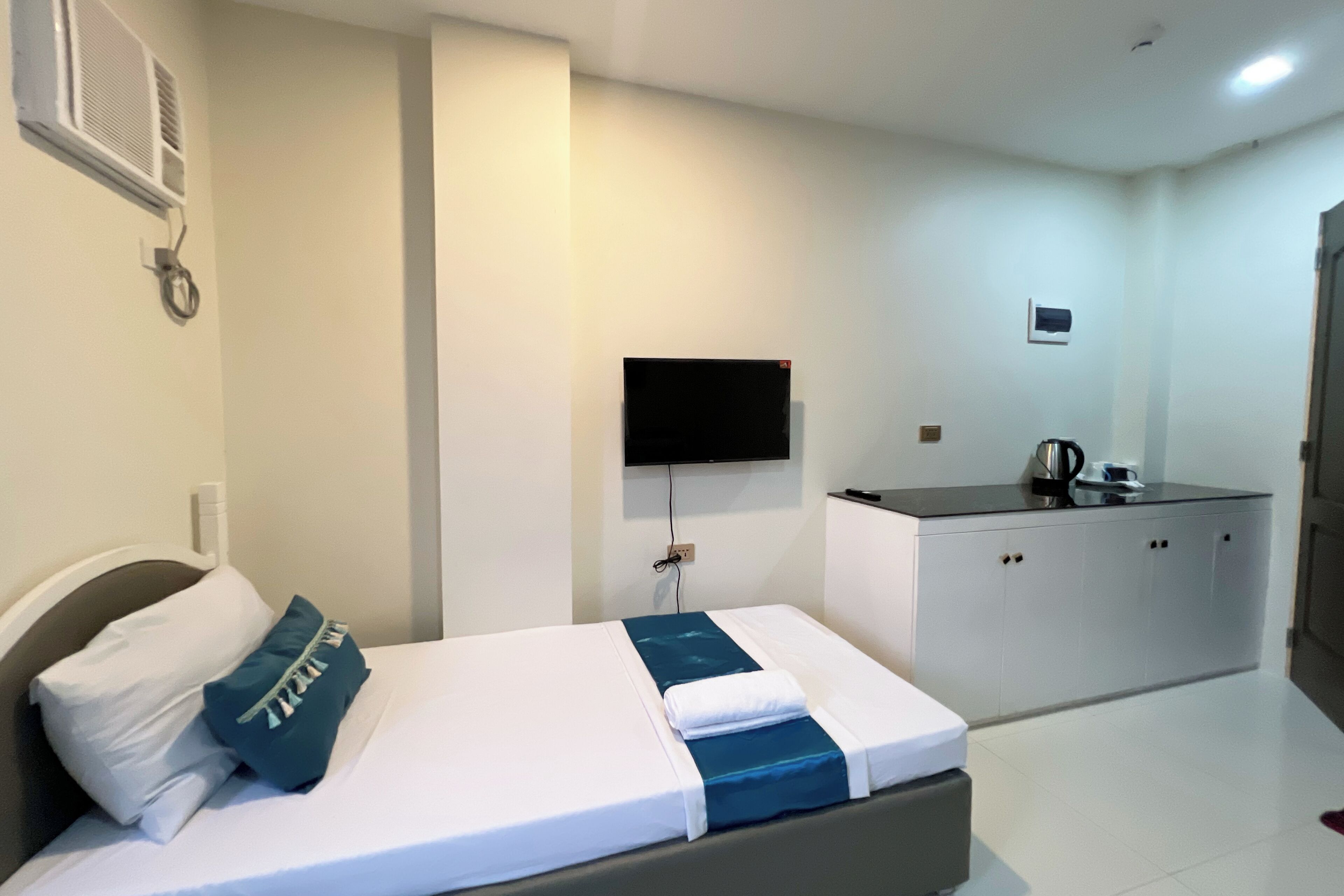 A hotel room with a bed, a TV mounted on the wall, a kitchenette, and a door.