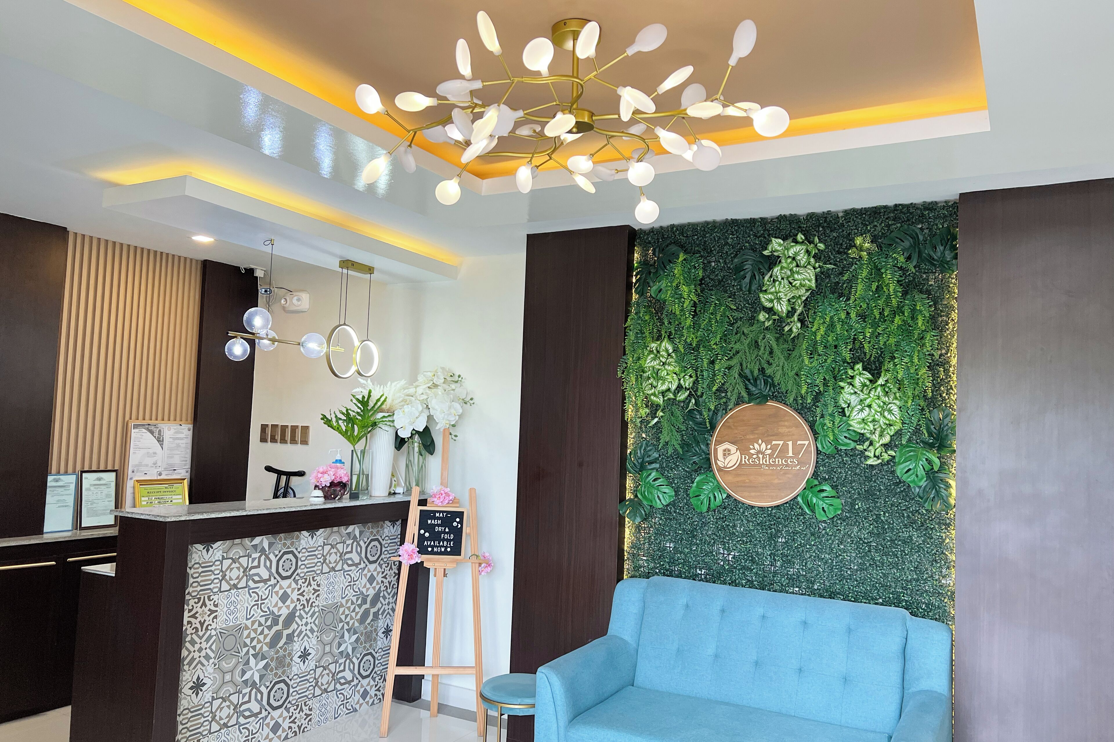 A reception area with a modern chandelier, a green wall with plants, a blue sofa, and a patterned tile backsplash.