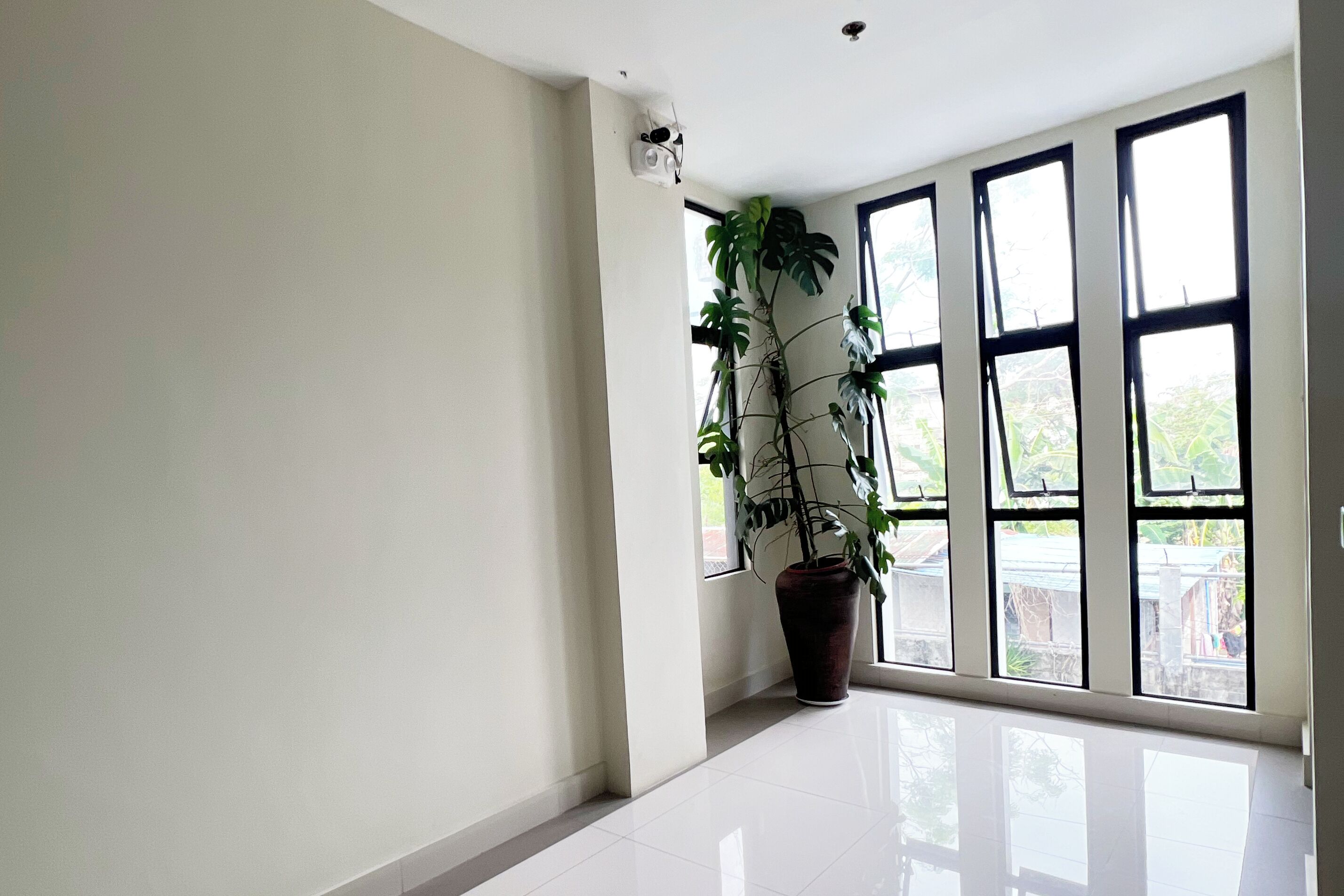 A spacious room with large windows, a potted plant, and a ceiling-mounted security camera.