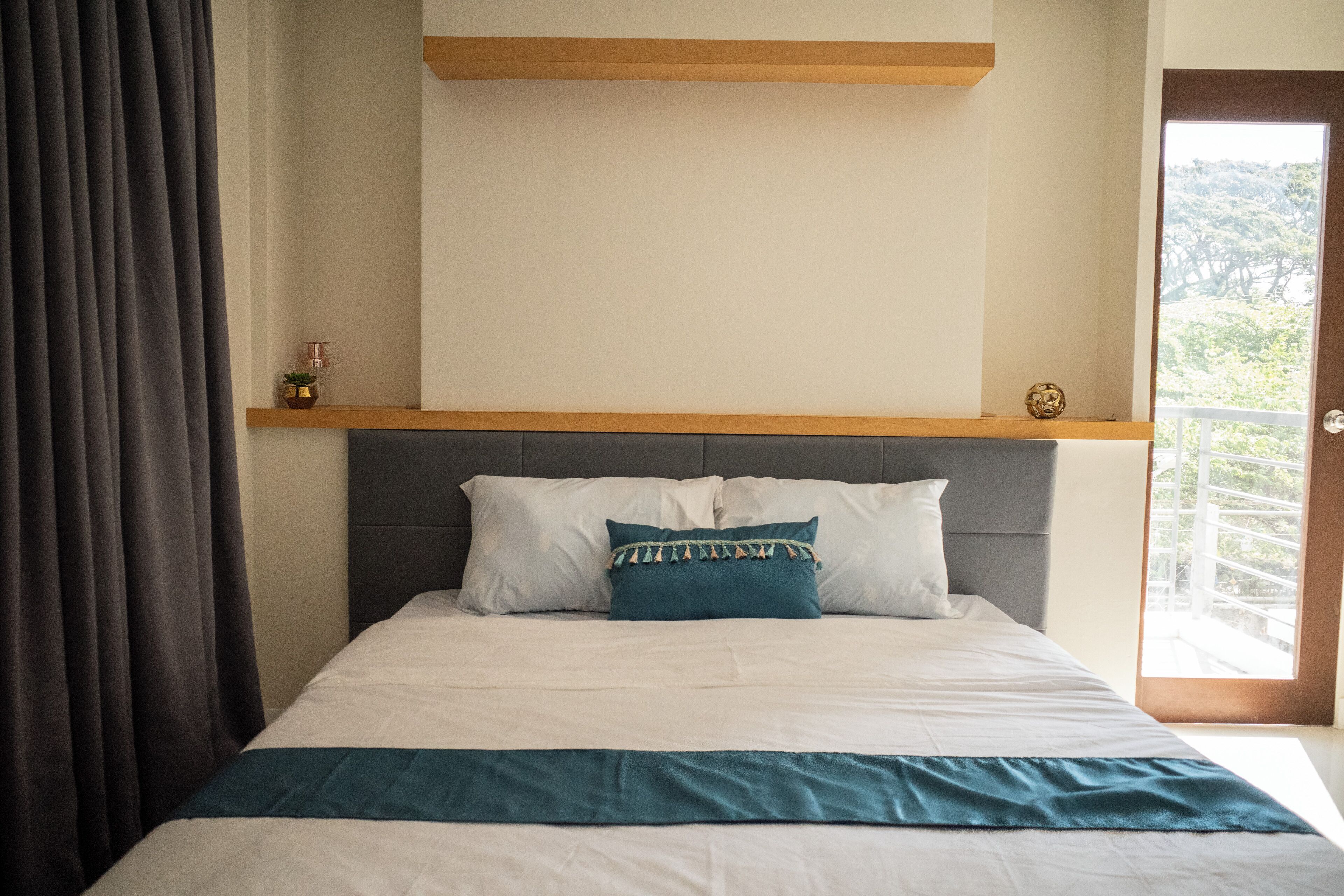 Ein ordentlich bezogenes Bett mit weißer und türkisfarbener Bettwäsche, ein Holz-Kopfschild und eine kleine Ablagefläche mit Pflanze und einem dekorativen Gegenstand.