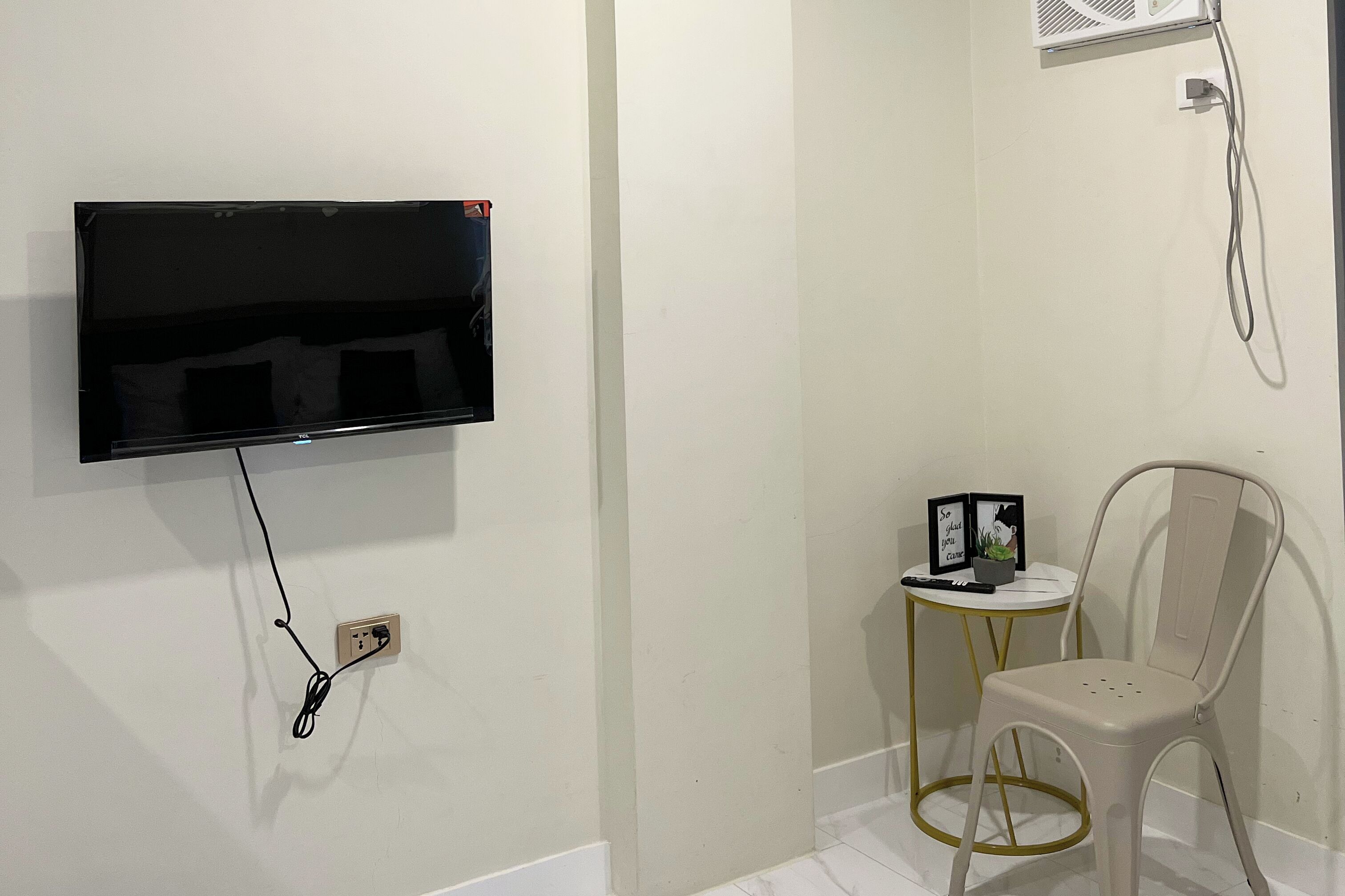 A bathroom with a mounted TV, a small table with a plant, and a chair.