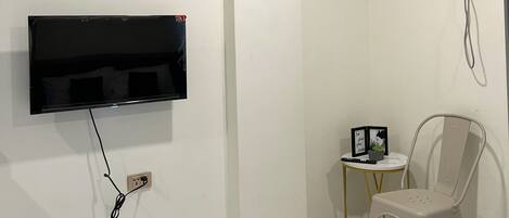 A bathroom with a mounted TV, a small table with a plant, and a chair.