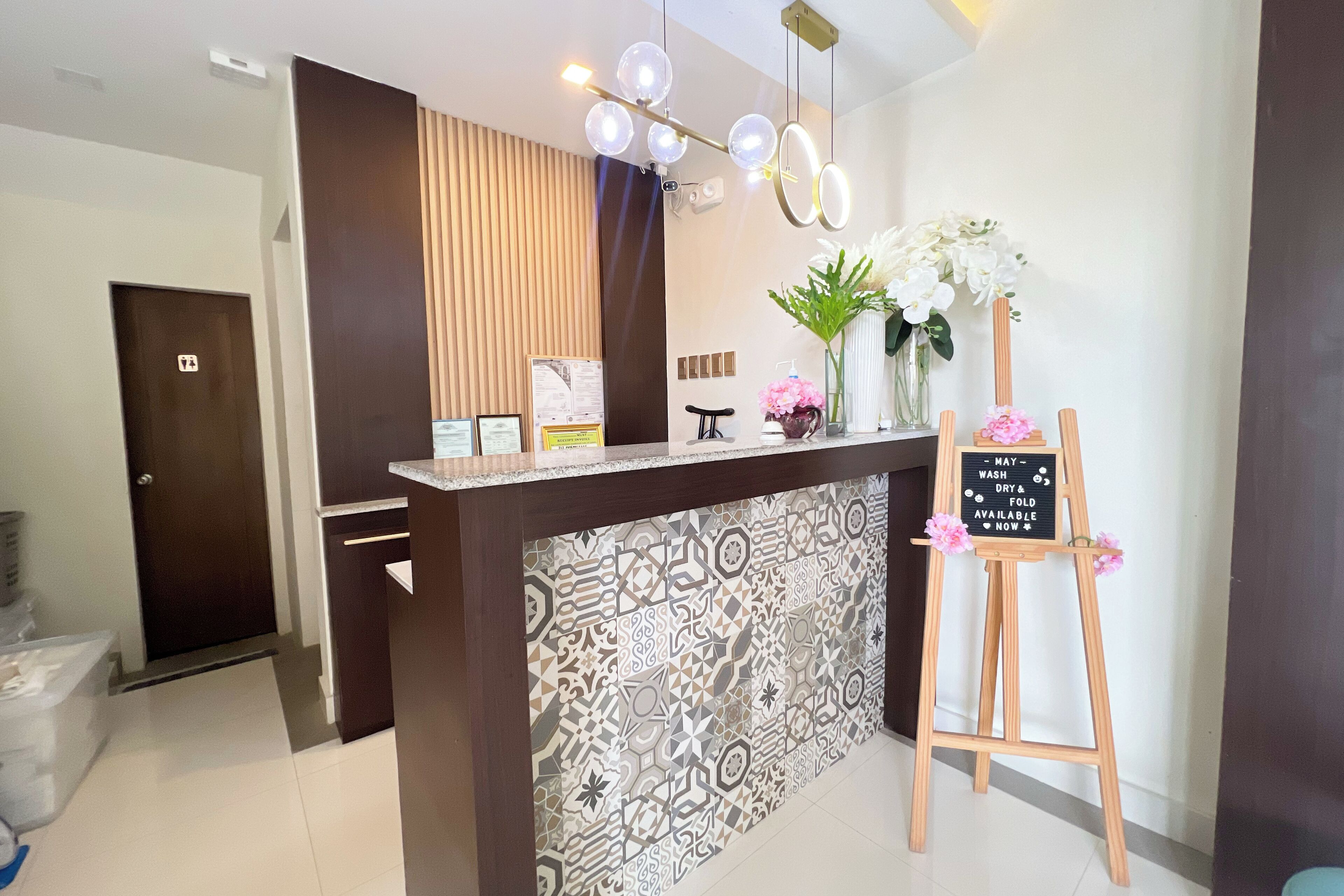 A reception area with a patterned tile wall, a wooden reception desk, a signboard, and a decorative plant.