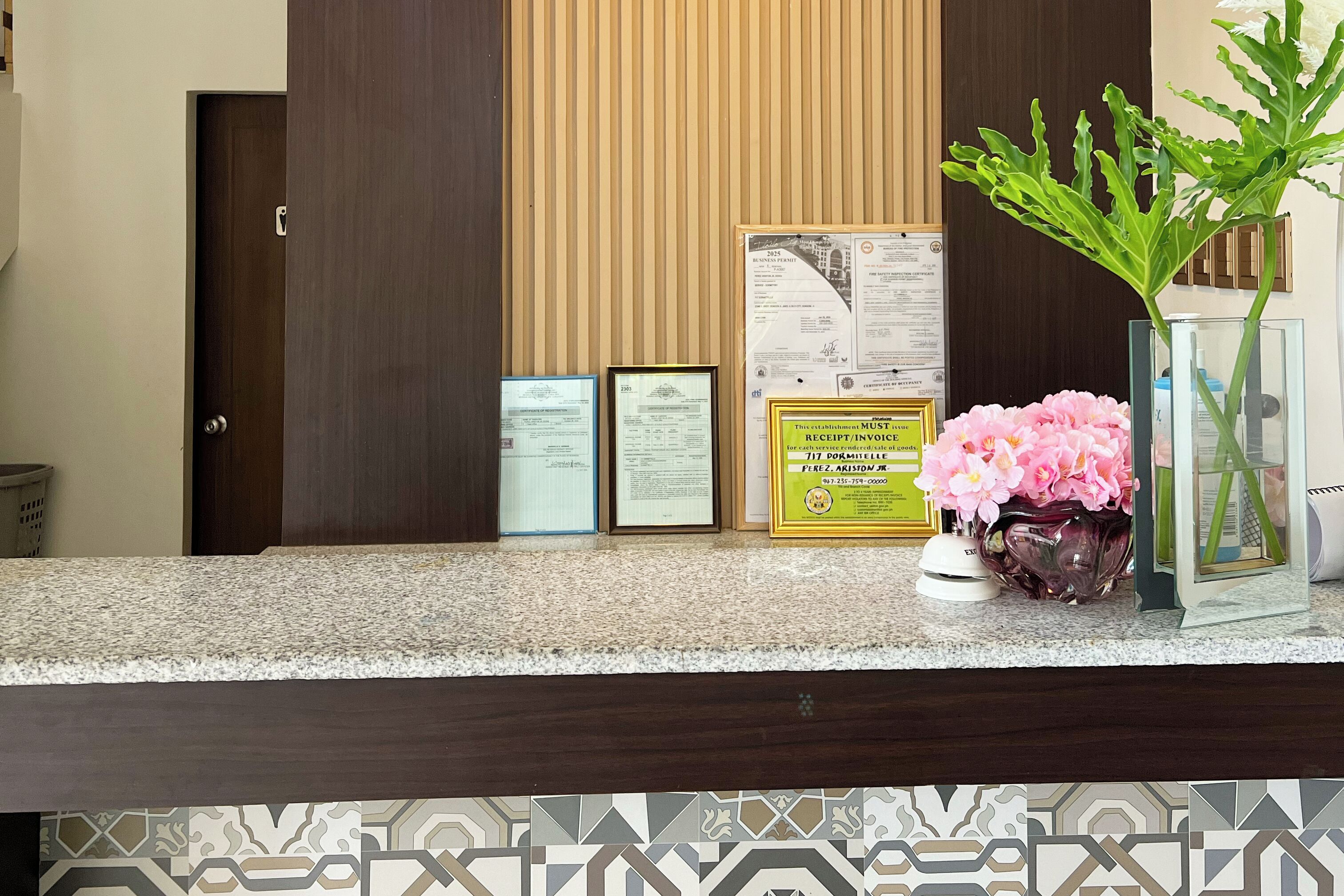 A reception desk with framed documents, a vase with flowers, and a glass display case.