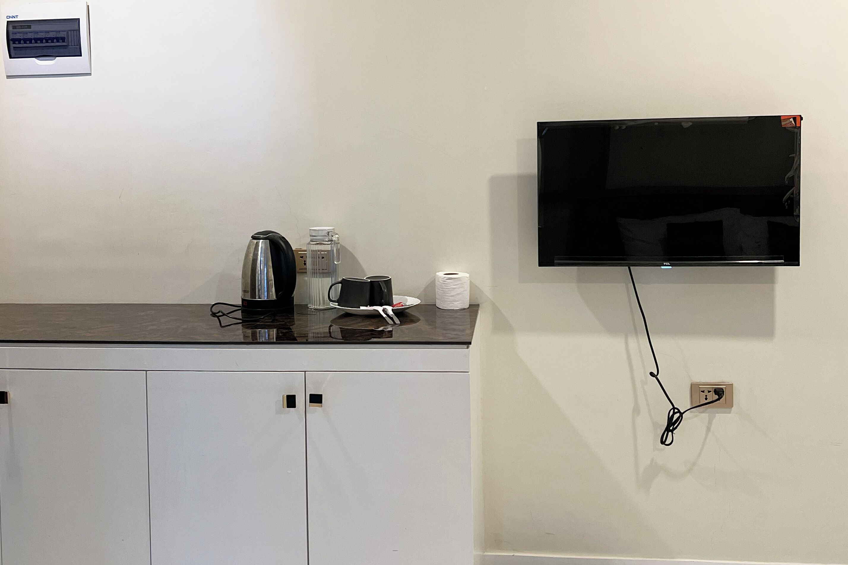 A kitchenette with a coffee maker, kettle, and a flat-screen TV mounted on the wall.