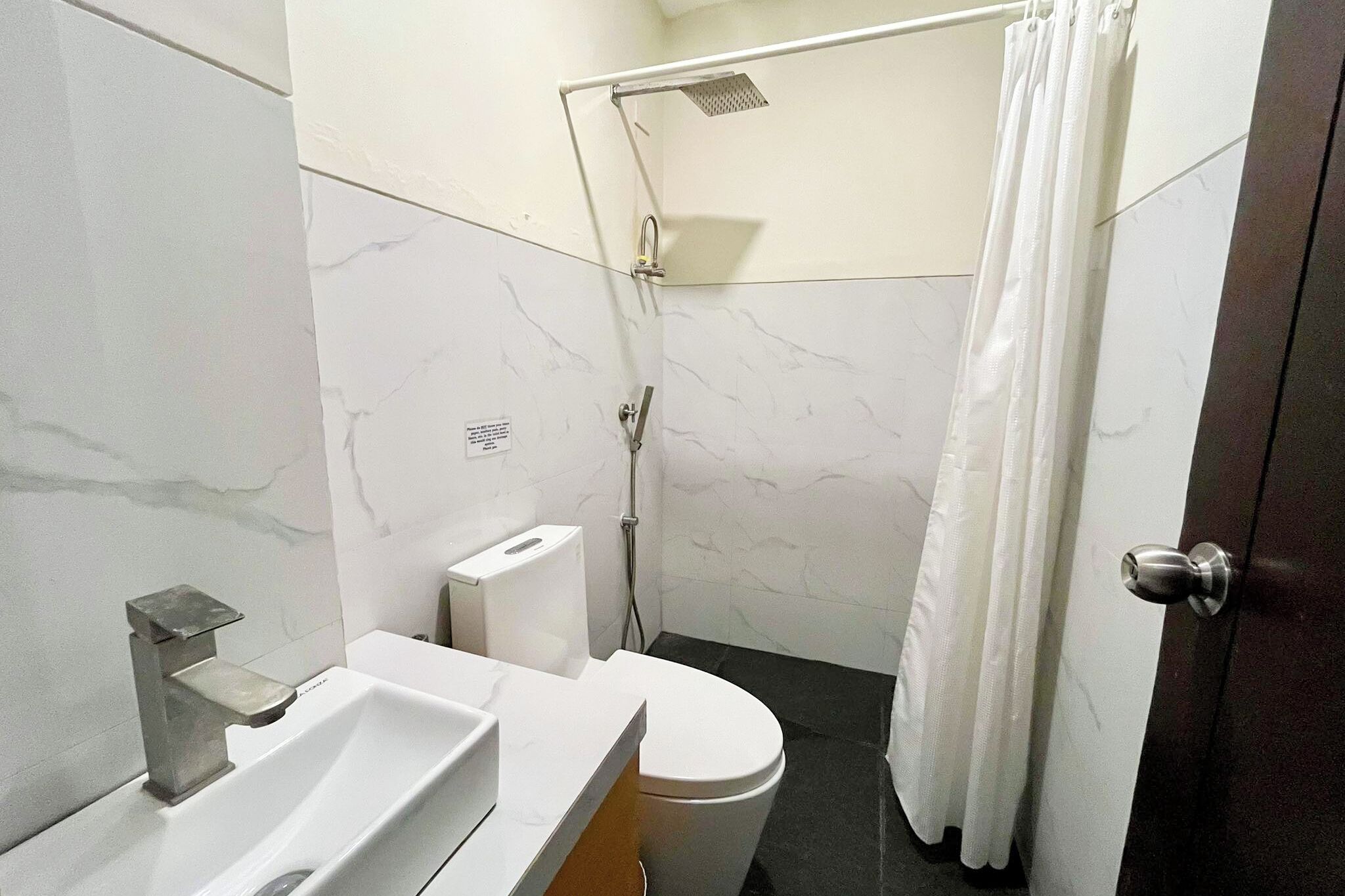 A bathroom with a white sink, a toilet, a shower with a curtain, and a door.