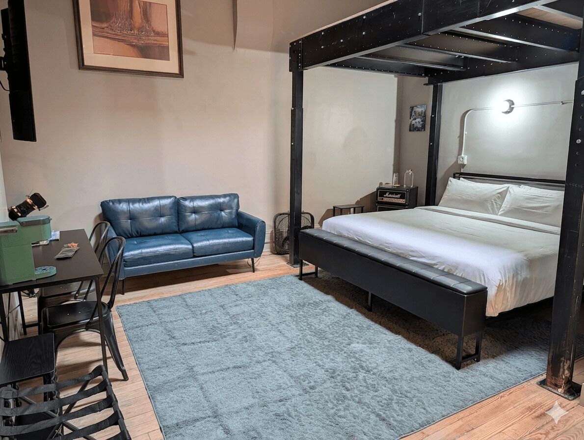 A bedroom with a four-poster bed, a desk with a chair, a blue sofa, and a small table with a lamp.