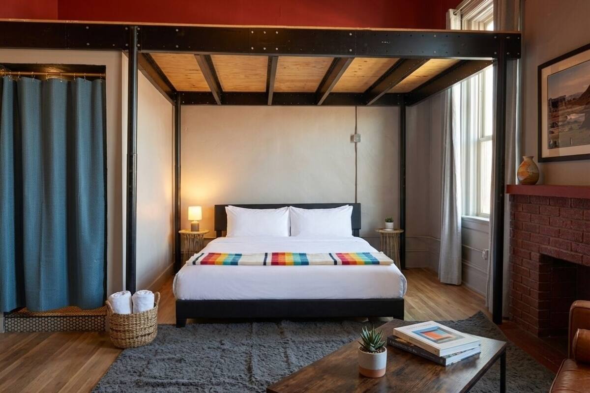 Habitación de hotel con cama, una mesita con una planta, chimenea y vistas al exterior.