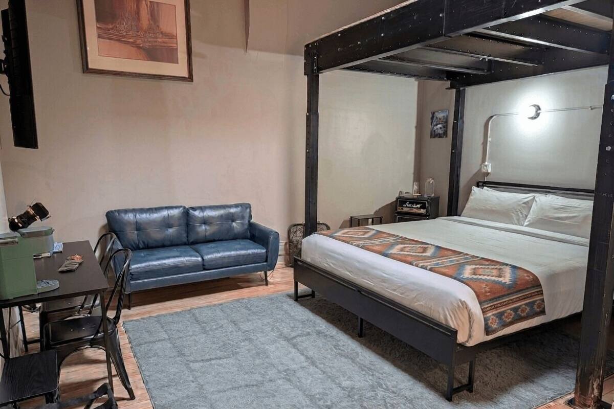 Un dormitorio con cama con dosel, un sofá azul, un escritorio con sillas y una mesita de noche con lámpara.