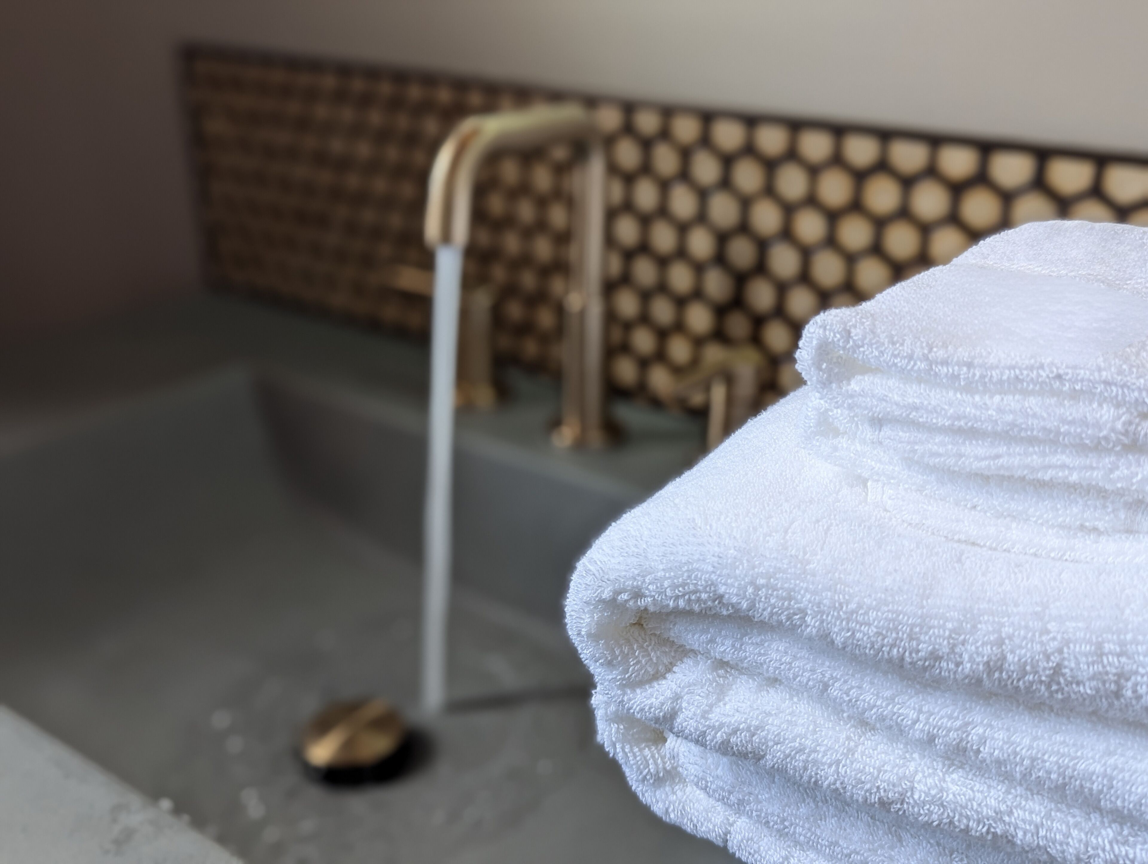 A bathroom with a bathtub, a faucet, and a stack of white towels.