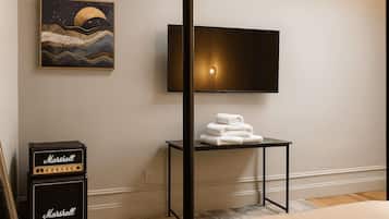 A hotel room with a flat-screen TV mounted on the wall, a small table with folded towels, a Marshall amplifier, and a painting of a moonlit sea.