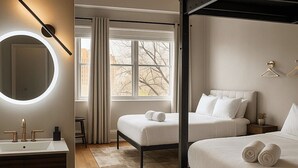 A modern hotel room with a large bed, a bedside table, a round mirror with lighting, a window with curtains, and a view of trees. - The Well Hotel & Taproom  (Trinidad)