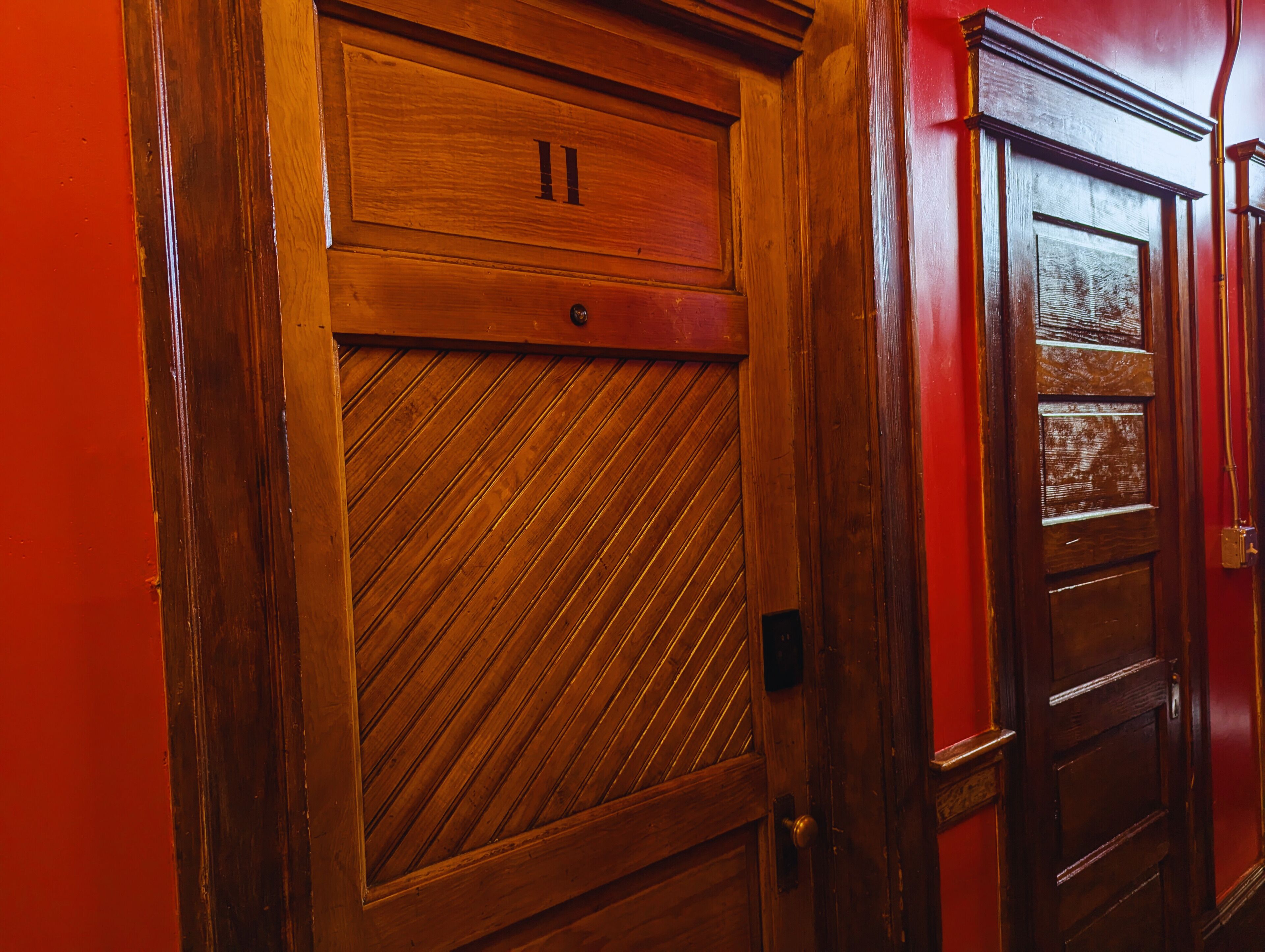 Une porte en bois ornée d’un motif à panneaux disposés en diagonale, avec le chiffre « 11 » au-dessus.