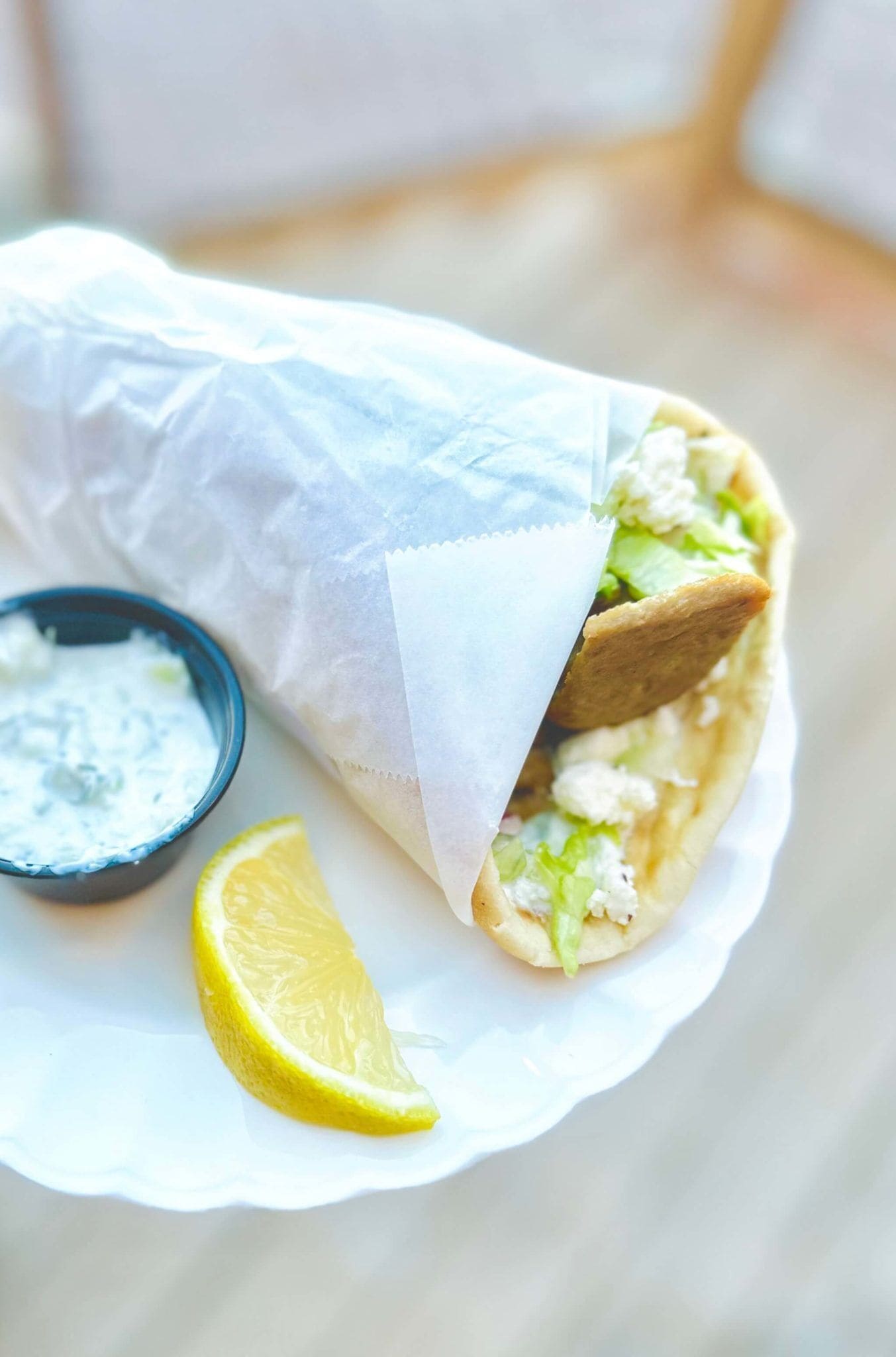 A wrap sandwich with lettuce and a side of tzatziki sauce, accompanied by a lemon wedge.