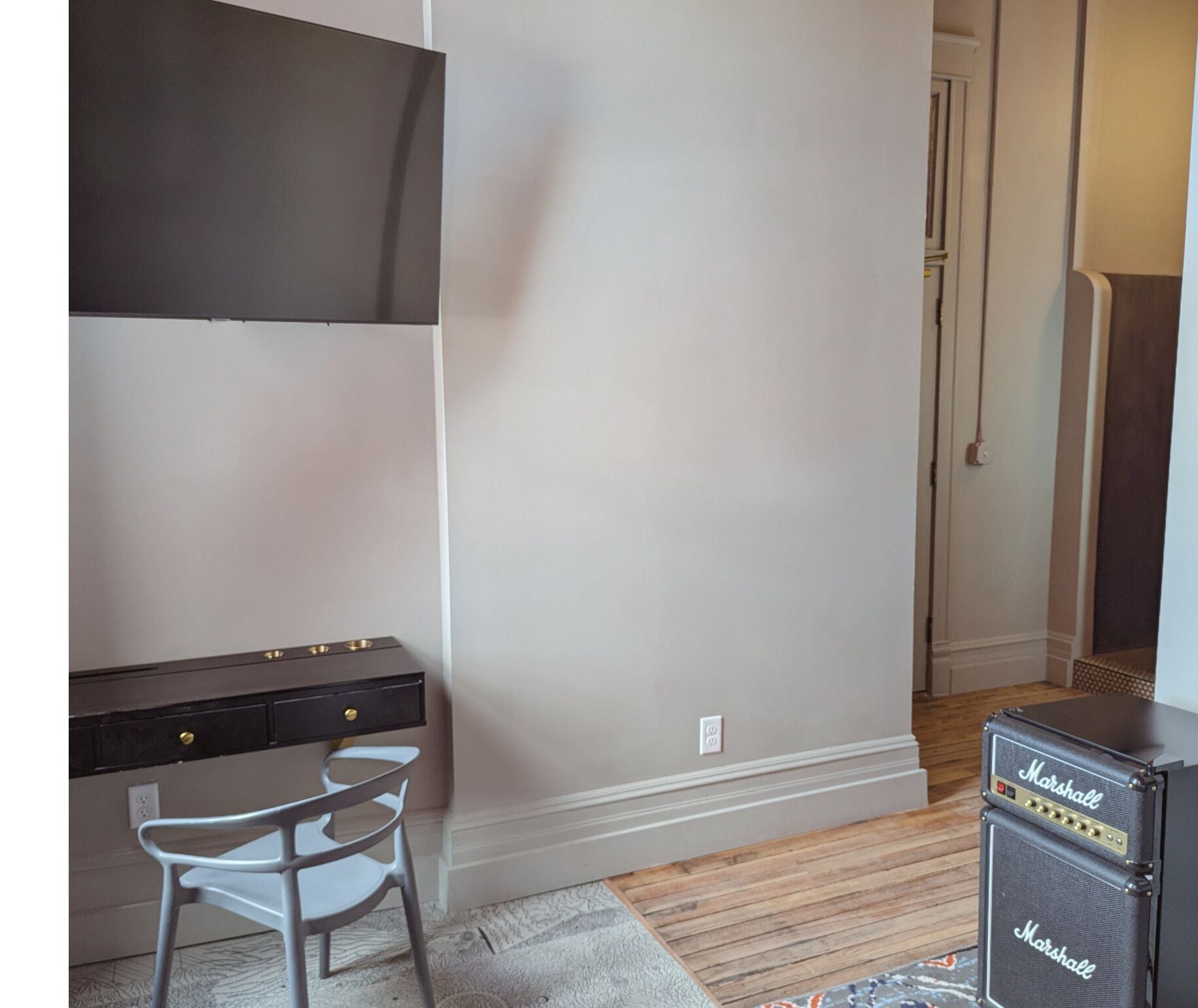 Una habitación con escritorio, una silla, un amplificador Marshall y una puerta que da a otra habitación.