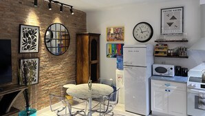 A modern kitchen with a refrigerator, oven, and microwave. There is a dining area with a table and chairs. The kitchen has a brick wall and a ceiling fan.