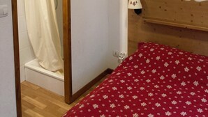A bedroom with a wooden headboard, a red floral bedspread, a white shower curtain, and a white wall.