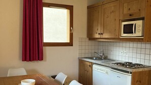A compact kitchen with wooden cabinets, a microwave, a dishwasher, and a dining area with a wooden table and chairs.
