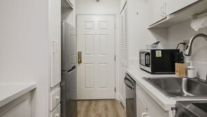 Una cocina compacta con armarios blancos, un lavamanos de acero inoxidable, un microondas y un refrigerador.