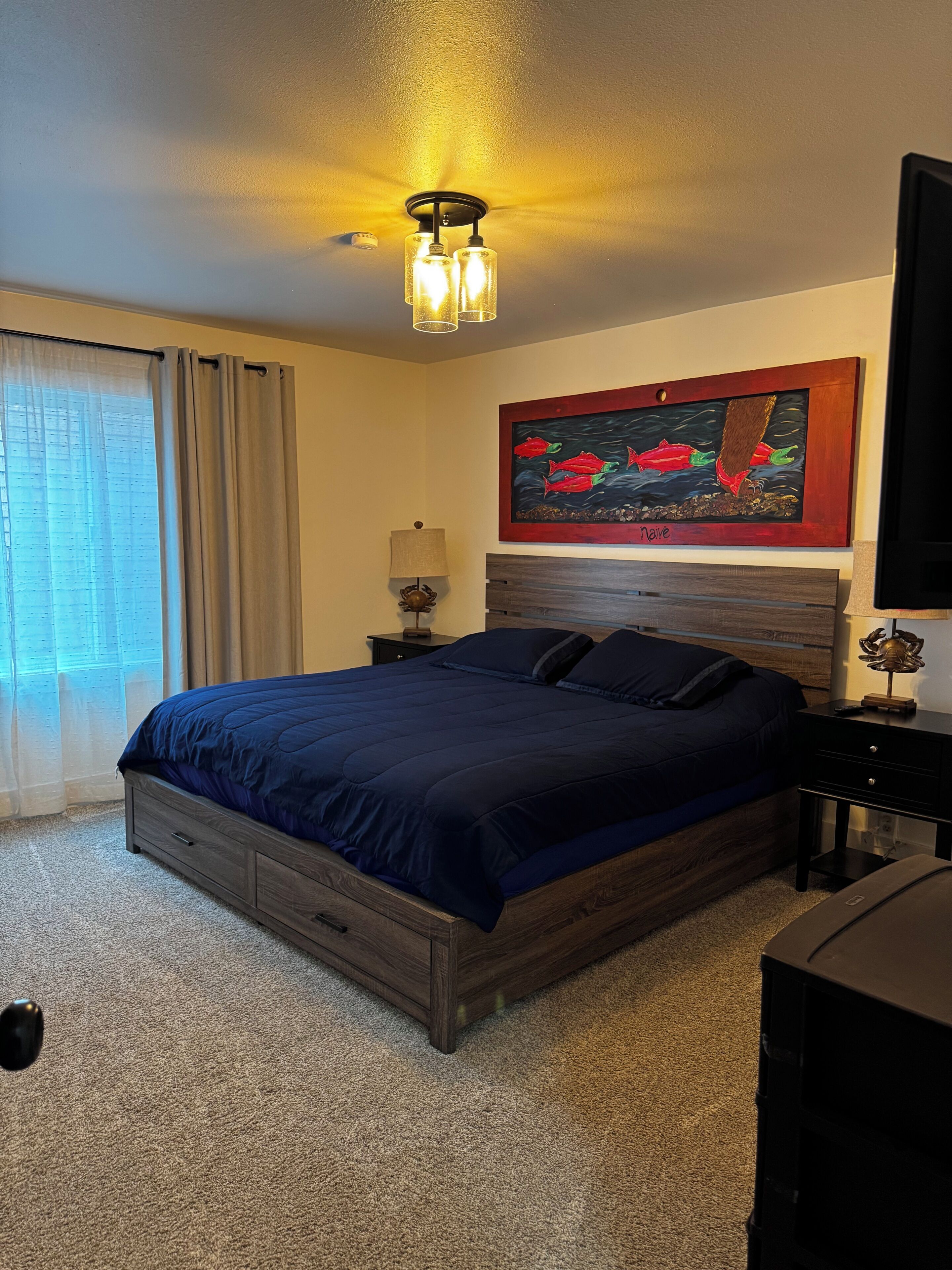 A bedroom with a bed, a nightstand, a lamp, a painting, and a ceiling light fixture.