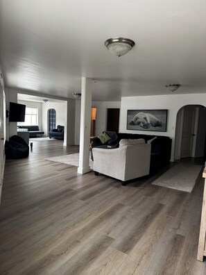 A spacious living area with a grey sofa, a flat-screen TV mounted on the wall, and a large window providing natural light. - Spacious 3-bedroom apartment in beautiful downtown Ketchikan (Ketchikan)