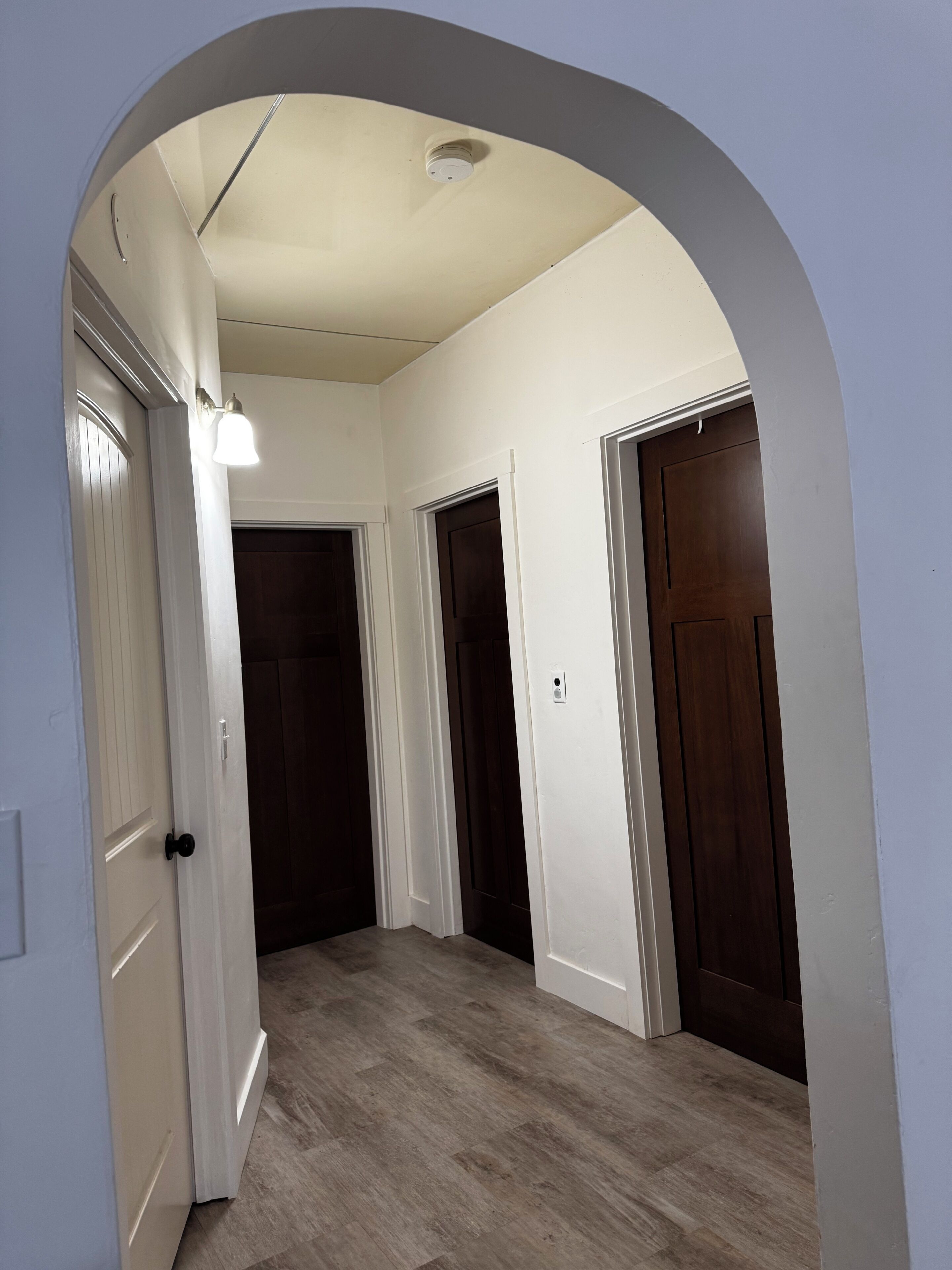 A hallway with a white archway, wooden flooring, and two closed doors.