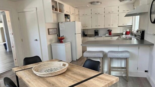 Une cuisine moderne avec des meubles blancs, une table à manger en bois et deux tabourets de bar.