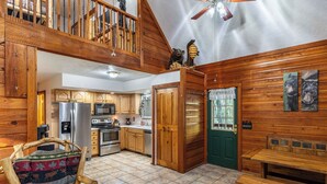 A rustic cabin interior with wooden walls, a dining area, a kitchen with modern appliances, and a loft bedroom.