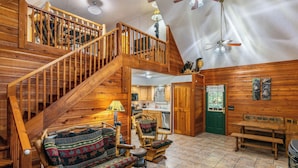 A wooden cabin interior with a staircase, wooden furniture, and a dining area.