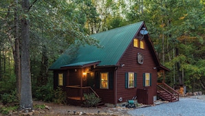 A rustic cabin with a green roof, wooden exterior, and a porch with a railing.