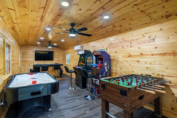 Ein Zimmer mit Holzboden, einer Tischfußballplatte, einem Billardtisch und zwei Arcade-Automaten.