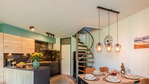 Une cuisine moderne dotée d’un îlot central, un coin repas avec une table et des chaises en bois, et un escalier en colimaçon menant à un niveau supérieur.