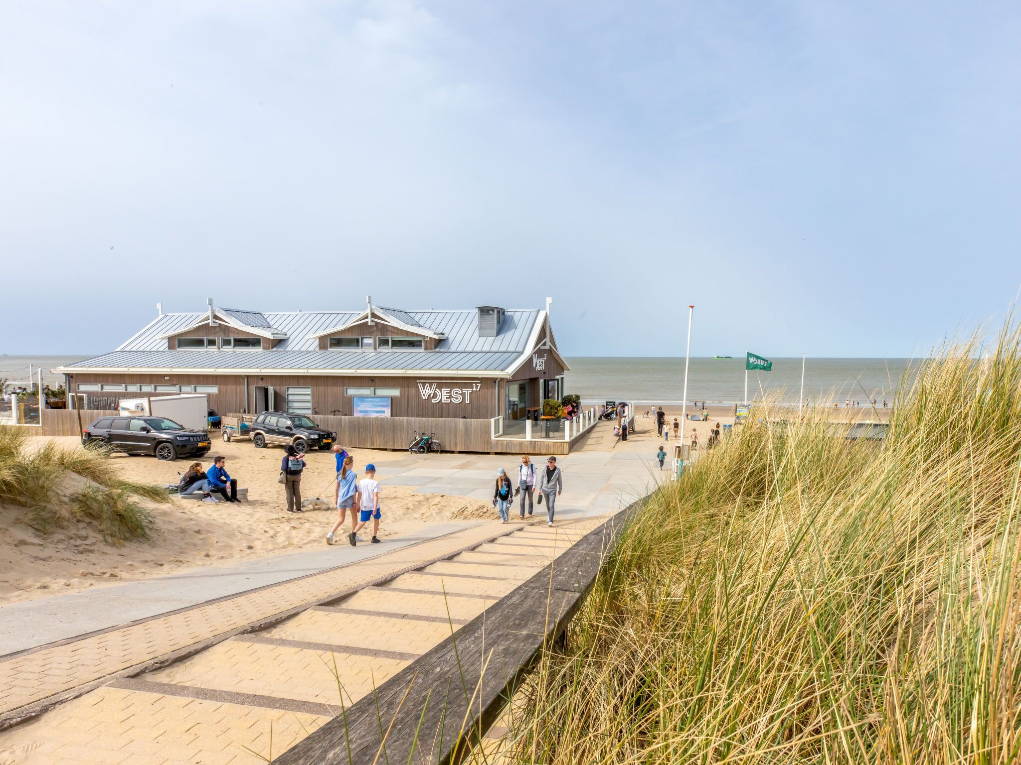 A beachside building with a 'WEST17' sign, a sandy pathway, and a grassy dune.