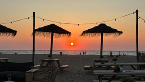 Un décor de plage avec des tables et des chaises en bois, ainsi que des parasols en chaume.