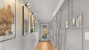 A hallway with framed artwork on the walls, a wooden floor, and a door leading to an outdoor area.
