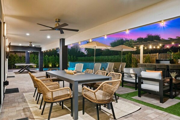 Une terrasse extérieure avec une table à manger, des chaises, un barbecue et des guirlandes lumineuses.