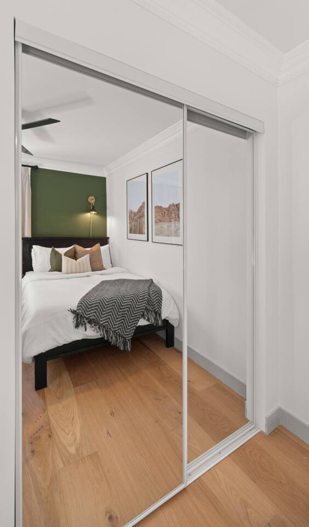 A bedroom with a bed, a green wall, a ceiling fan, and framed pictures.