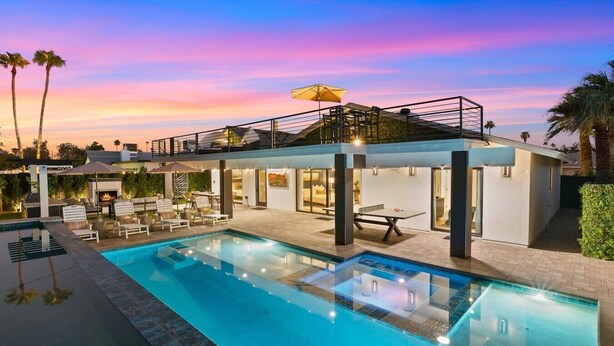A modern outdoor pool area with lounge chairs, a table, and a covered seating area.