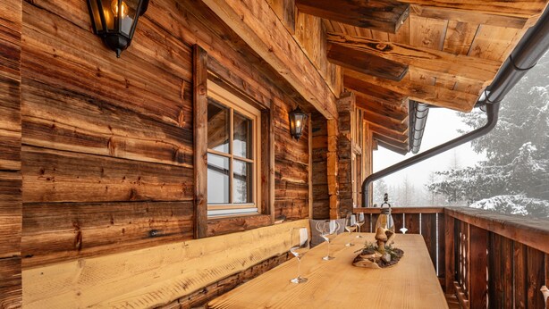 A wooden cabin with a wooden deck, a bench, and a table with wine glasses. - Heregger Hütte by Interhome (Dellach)