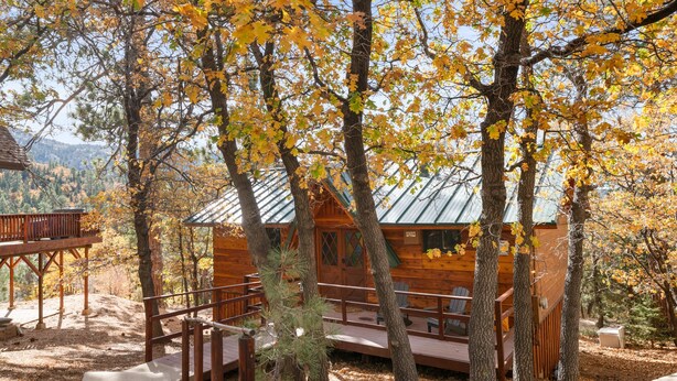 Una cabaña con fachada de madera, techo de metal y una terraza con sillas.