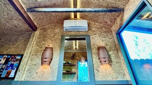 A room with a sloped ceiling, wooden paneling, a central air conditioning unit, a built-in shelf with decorative items, and a window on the right side. - Pet Friendly Fully Fenced Cozy Casita near Sedona! (Lake Montezuma)