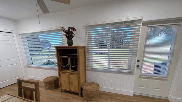 A room with a wooden cabinet, wicker ottomans, a dining table, and a door with a window.