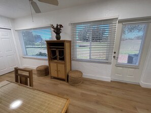 Een kamer met een houten kast, rieten poefs, een eettafel en een deur met een raam.