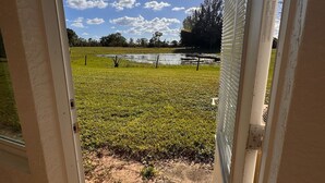 An open door leading to a grassy area with a pond and trees in the background.