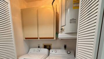 A compact laundry room with two front-loading washers and dryers, wooden cabinets above, and a caution sign on the wall.