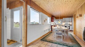 Une cuisine moderne avec des meubles en bois, un coin repas comprenant une table et des chaises, et une vue sur l’extérieur grâce à de grandes fenêtres.