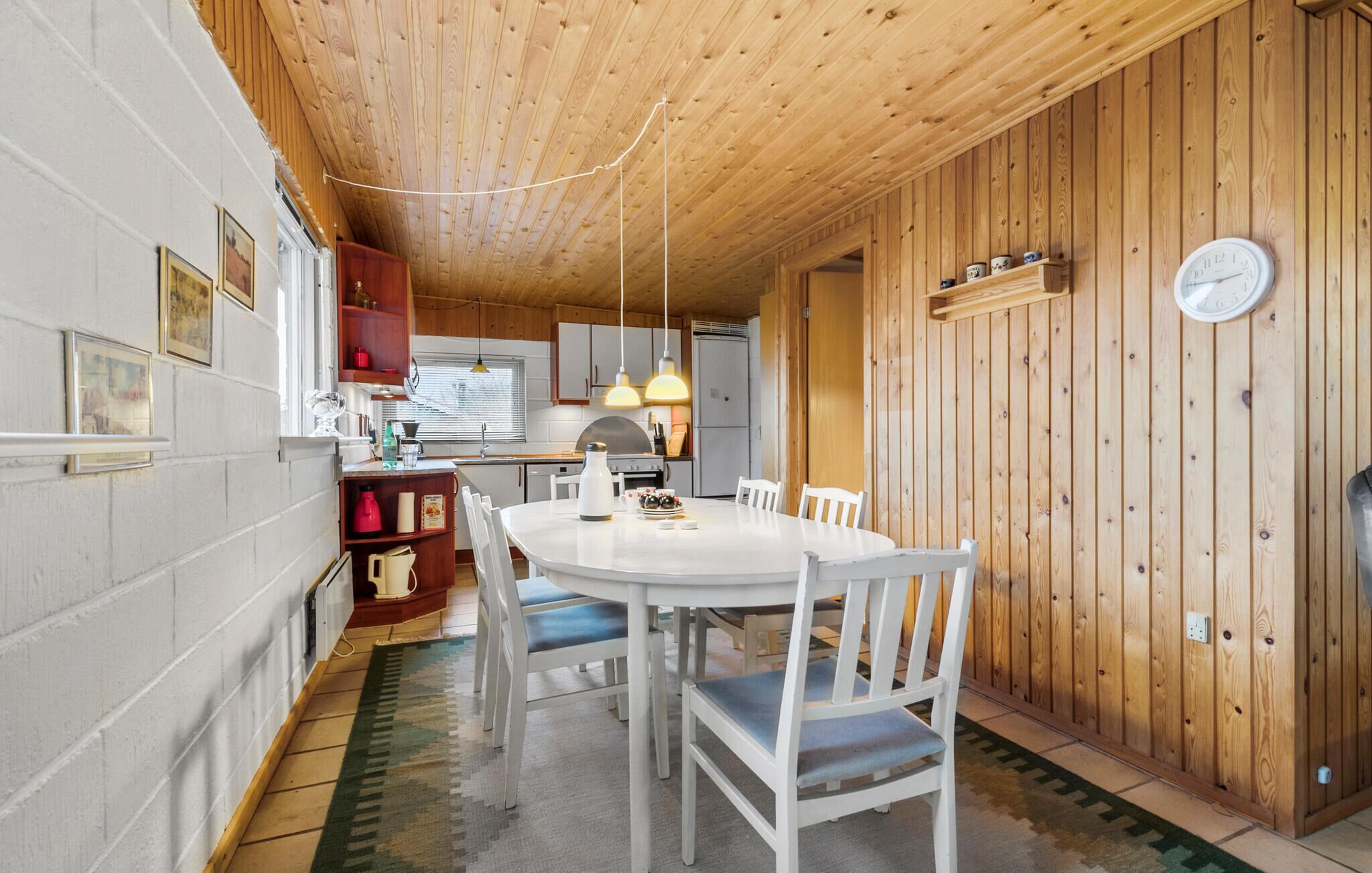 Een kleine keuken met witte kastjes, een ronde eettafel met witte stoelen en een houten plafond.