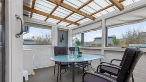 Une terrasse couverte avec une table ronde en verre, deux chaises et une bouteille d’eau.