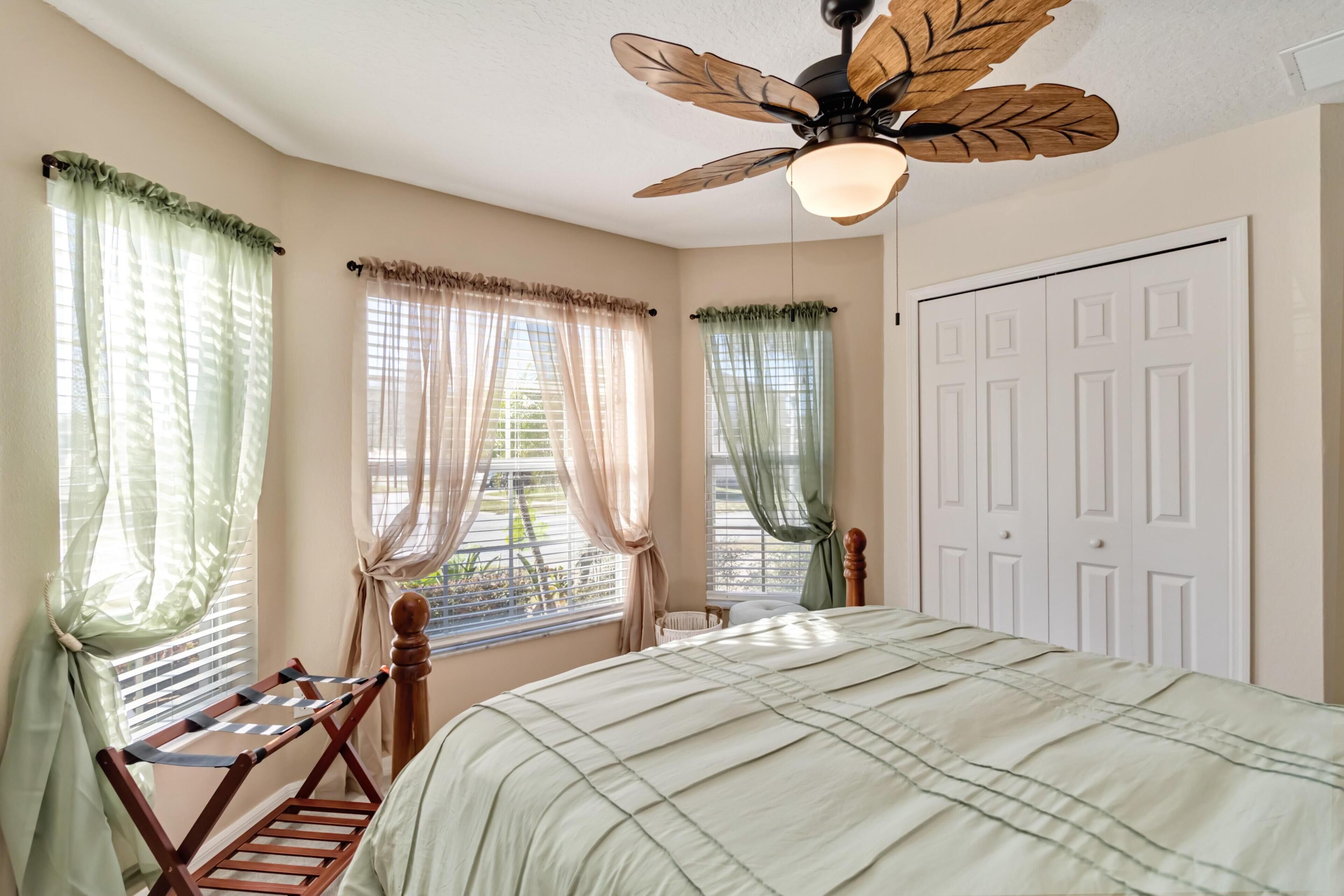 A bedroom with a bed, a ceiling fan, and two windows with curtains.